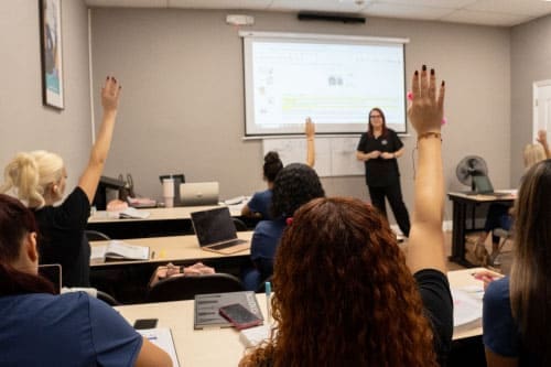 FAMA students raising their hands during a classroom lecture with instructor teaching at the front