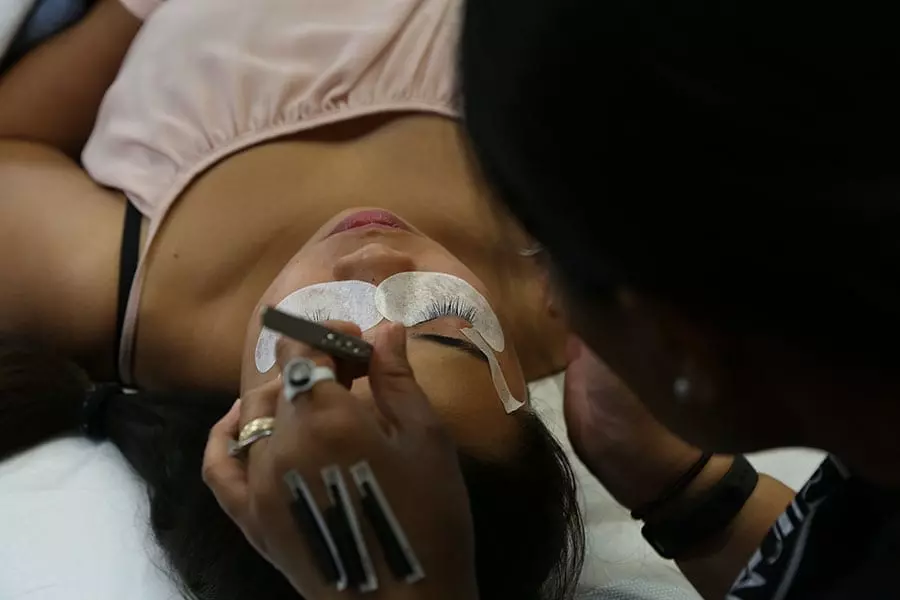 FAMA student applying eyelash extensions to a model in the training clinic